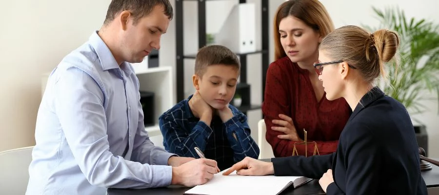 Man signing paper in front of child and lawyer